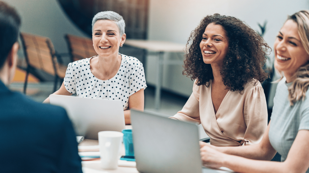 This image shows coworkers laughing at a meeting. Edgility's Total Rewards and Benefits Service helps organizations create total compensation strategies that meet the needs of their staff.